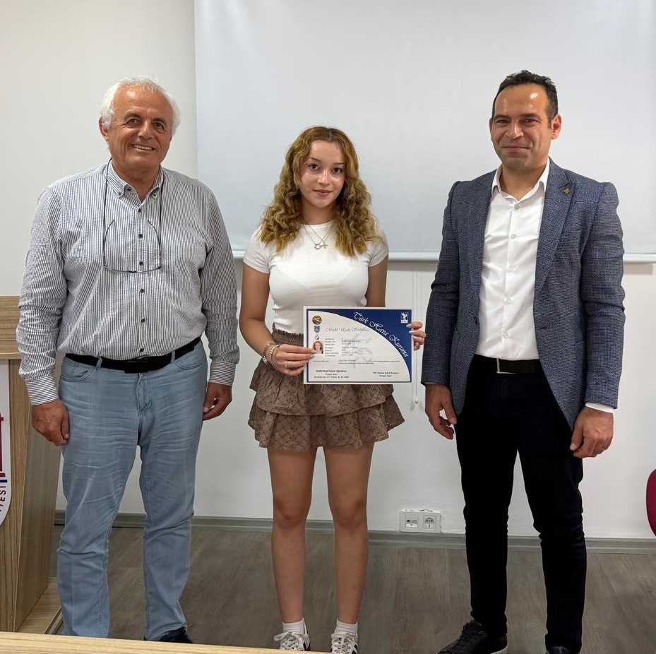THK Ortaca Şubesi Başkanı Cengiz Şatır ve Dalaman MYO Müdürü Doç. Dr. Ozan Kaya, genç bir kadın öğrenciye sertifikasını takdim ederken görülüyor. Öğrenci, elinde Türk Hava Kurumu logolu bir sertifikayla iki yetkilinin arasında duruyor.
